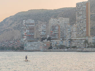 Rückenansicht von unkenntlich sportlichen Mann Schwimmen auf Surfbrett Paddel Blick auf erstaunliche Stadtbild in Alicante Spanien - ADSF40200
