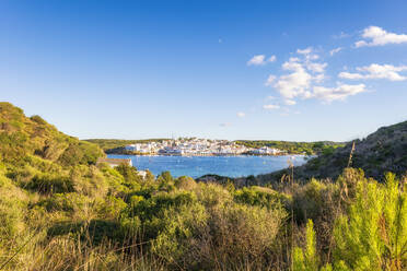 Spanien, Balearische Inseln, Menorca, Küstendorf von einem grasbewachsenen Hügel aus gesehen im Sommer - SMAF02341