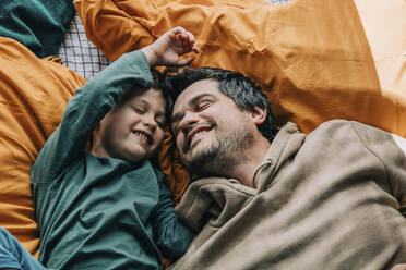 Smiling boy with father lying on bed at home - VSNF00071