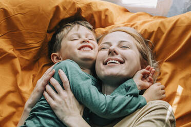 Lächelnder Junge mit Mutter zu Hause auf dem Bett liegend - VSNF00073