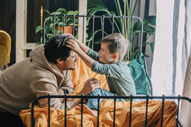 Son adjusting father's hair on bed at home - VSNF00074