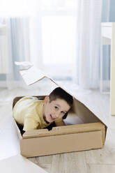 Lächelnder Junge versteckt sich zu Hause in einer Schachtel - ONAF00230