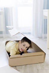 Smiling boy hiding in box at home - ONAF00230