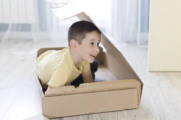Niedlicher verspielter Junge versteckt sich in einem Karton zu Hause - ONAF00231