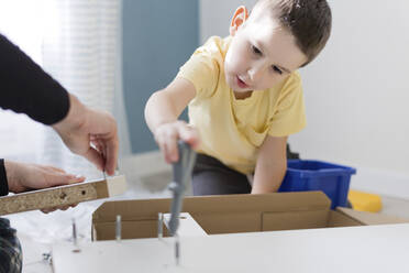 Junge hilft Vater beim Zusammenbau eines Tisches zu Hause - ONAF00234
