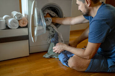Mann beim Einlegen von Kleidung in die Waschmaschine zu Hause - ANAF00420