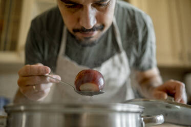 Man examining onion on spoon at home - ANAF00430