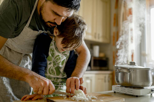 Vater lehrt Sohn in der Küche Zwiebeln zu hacken - ANAF00434