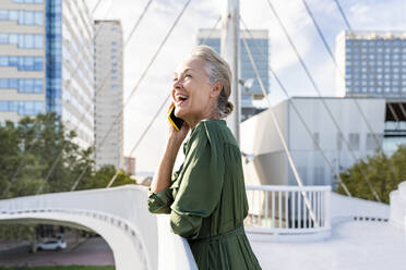 Glückliche Frau, die in der Nähe des Geländers mit einem Smartphone spricht - OIPF02655