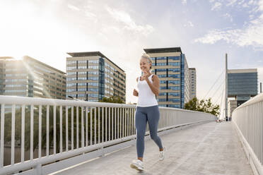 Mature woman jogging on footbridge in city - OIPF02678