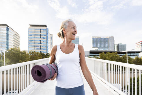 Happy woman with exercise mat on footbridge - OIPF02681