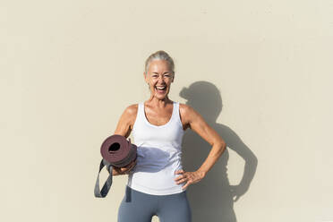 Glückliche Frau mit Hand auf der Hüfte vor einer cremefarbenen Wand an einem sonnigen Tag - OIPF02685