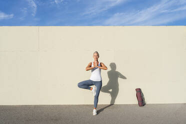 Frau übt Yoga vor einer cremefarbenen Wand an einem sonnigen Tag - OIPF02687