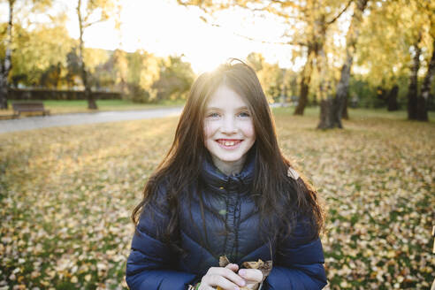 Smiling girl wearing warm clothing standing in autumn park - EYAF02310