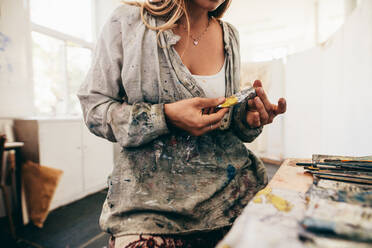 Ausschnitt einer Frau, die in ihrem Atelier eine Farbröhre hält, Nahaufnahme einer Künstlerin, die mit Farben hantiert. - JLPSF27310
