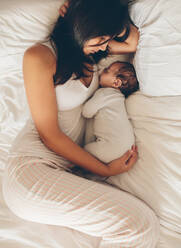 Mutter und Sohn schlafen auf dem Bett. Junge Frau mit neugeborenem Jungen im Bett zu Hause. - JLPSF27326