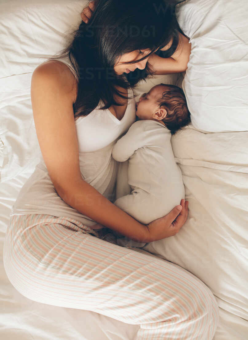 Free Photo  Young beautiful happy mother in sleepwear and her newborn baby  sitting on bed in morning smiling playing together.