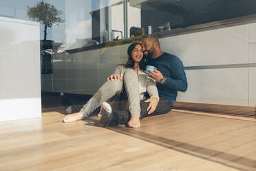 Glücklicher junger Mann und Frau sitzen auf dem Küchenboden. Romantisches junges Paar sitzt morgens auf dem Küchenboden. - JLPSF27329