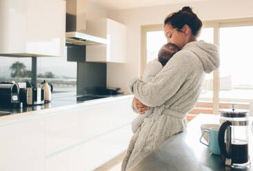 Mutter im Bademantel, die ein Baby im Arm hält. Frau mit ihrem Sohn in der Küche am Morgen. - JLPSF27334