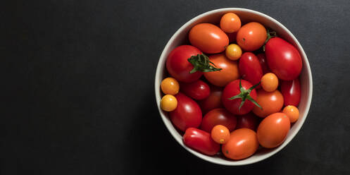 Bowl containing tomatoes placed on a black background. Sea berries along with tomatoes in a bowl. - JLPSF27357