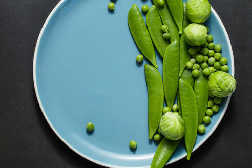 Grüne Erbsen und Rosenkohl auf einem blauen Teller auf schwarzem Hintergrund. - JLPSF27359