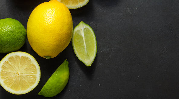 Geschnittene und ungeschnittene Limetten und Zitronen auf schwarzem Hintergrund, Draufsicht auf Limetten und Zitronen auf dem Tisch. - JLPSF27372