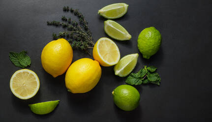 Cut and uncut limes and lemons on a black background along with mint leaves. - JLPSF27373