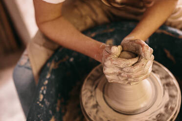 Töpferin bei der Herstellung eines Tontopfs auf der Töpferscheibe in einer Werkstatt. Handwerkerin, die Ton mit den Händen auf der Töpferscheibe formt. - JLPSF27378