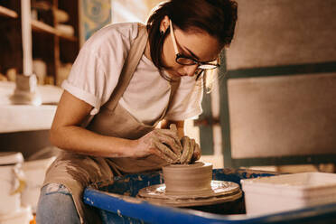 Frau, die Ton auf einer Töpferscheibe formt. Handwerkerin, die in einer Werkstatt einen Topf herstellt. - JLPSF27382