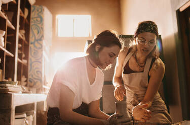 Töpferin unterrichtet eine Frau im Töpferhandwerk. Junge Frau lernt in der Werkstatt, Ton auf der Töpferscheibe zu formen. - JLPSF27395