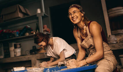 Zwei Frauen, die in einer Werkstatt Tontöpfe auf der Töpferscheibe herstellen. Fröhliche Frauen, die in einer Töpferwerkstatt die Kunst des Töpferns genießen. - JLPSF27401