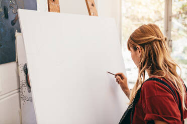 Innenaufnahme einer jungen Frau, die auf einer Leinwand skizziert. Eine Malerin zeichnet in ihrem Atelier. - JLPSF27410