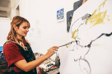 Creative female painter paints a colorful picture on canvas in workshop. Woman artist making a painting in her studio. - JLPSF27414