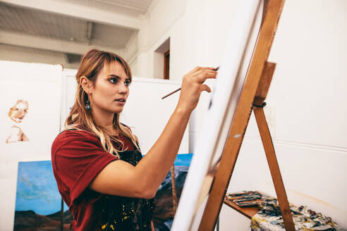 Schöne Künstlerin beim Zeichnen an der Staffelei. Malerin beim Malen auf Leinwand in ihrem Atelier. - JLPSF27415