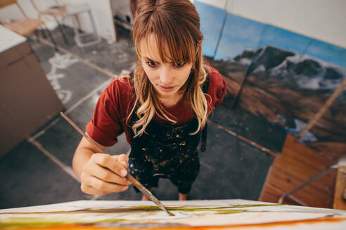 Blick von oben auf eine junge Künstlerin, die in einem Atelier ein Bild malt. Eine Frau malt auf einer Leinwand. - JLPSF27416