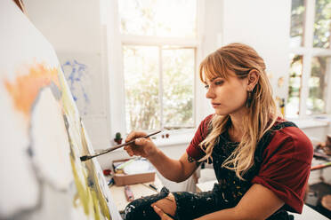 Innenaufnahme einer kreativen jungen Frau, die in ihrem Atelier auf einer Leinwand malt. Künstlerin in ihrer Werkstatt. - JLPSF27418