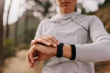 Nahaufnahme einer Sportlerin, die ihren Fitnessfortschritt auf ihrer Smartwatch überprüft. Eine Läuferin nutzt eine Fitness-App, um ihre Trainingsleistung zu überwachen. - JLPSF27421