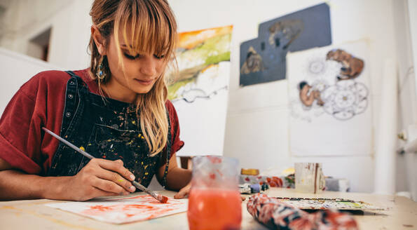 Aufnahme einer schönen jungen Künstlerin, die im Atelier malt. Eine Malerin, die in ihrem Atelier auf Papier zeichnet. - JLPSF27429
