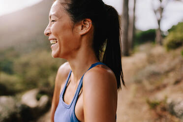 Seitenansicht einer fitten jungen Frau, die im Freien steht, wegschaut und lacht. Glückliche Läuferin in Sportkleidung am Morgen. - JLPSF27443