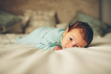 Süßes kleines Baby auf dem Bett liegend. Kleines Baby liegt auf dem Bauch und schaut in die Kamera. - JLPSF27453