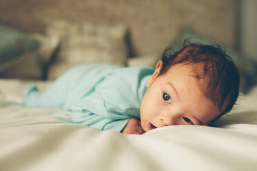 Süßes kleines Baby auf dem Bett liegend, kleiner Junge auf dem Bauch liegend. - JLPSF27454