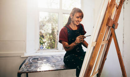 Aufnahme einer jungen kaukasischen Malerin bei der Arbeit in ihrem Atelier. Kreative junge Frau malt in ihrem Atelier auf Leinwand. - JLPSF27475