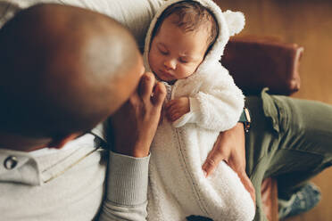 Draufsicht auf einen kleinen Jungen, der in den Armen seines Vaters schläft. Neugeborener Sohn mit Vater auf dem Sofa zu Hause. - JLPSF27476