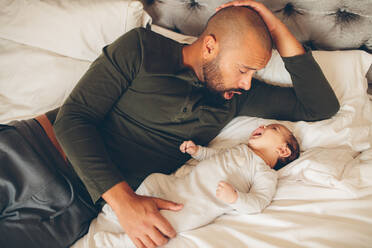 Glücklicher Vater mit seinem Sohn, der zu Hause auf dem Bett spielt. Mann und kleiner Babyjunge im Schlafzimmer. - JLPSF27478