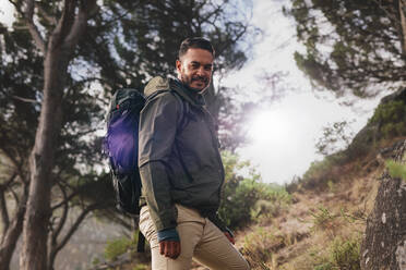 Porträt eines gutaussehenden jungen Mannes mit Rucksack auf einem Bergpfad. Kaukasischer Mann beim Wandern in der Natur. - JLPSF27479