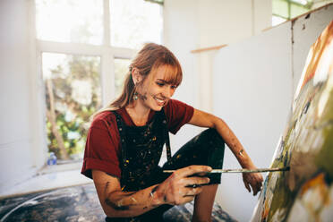 Innenaufnahme einer professionellen Künstlerin, die im Atelier auf einer Leinwand malt. Eine Frau malt in ihrer Werkstatt. - JLPSF27480