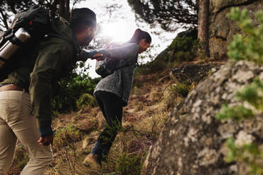 Wanderin hilft ihrem Freund beim Bergaufgehen in der Natur. Junges Paar beim Wandern in den Bergen. - JLPSF27481