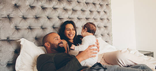 Glückliche Eltern spielen mit ihrem neugeborenen Sohn auf dem Bett zu Hause. Ehepaar mit kleinem Baby auf dem Bett. - JLPSF27482