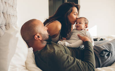 Eltern mit ihrem neugeborenen Baby auf dem Bett zu Hause. Frau küsst ihren Sohn sitzt mit Vater. - JLPSF27484