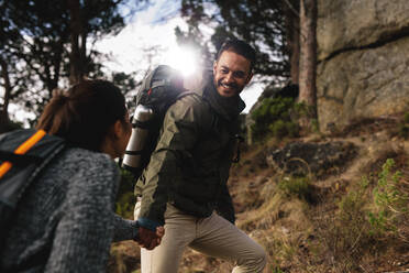 Wanderer hilft seiner Freundin auf einem Feldweg bergauf. Junges Paar beim Wandern in den Bergen. - JLPSF27487